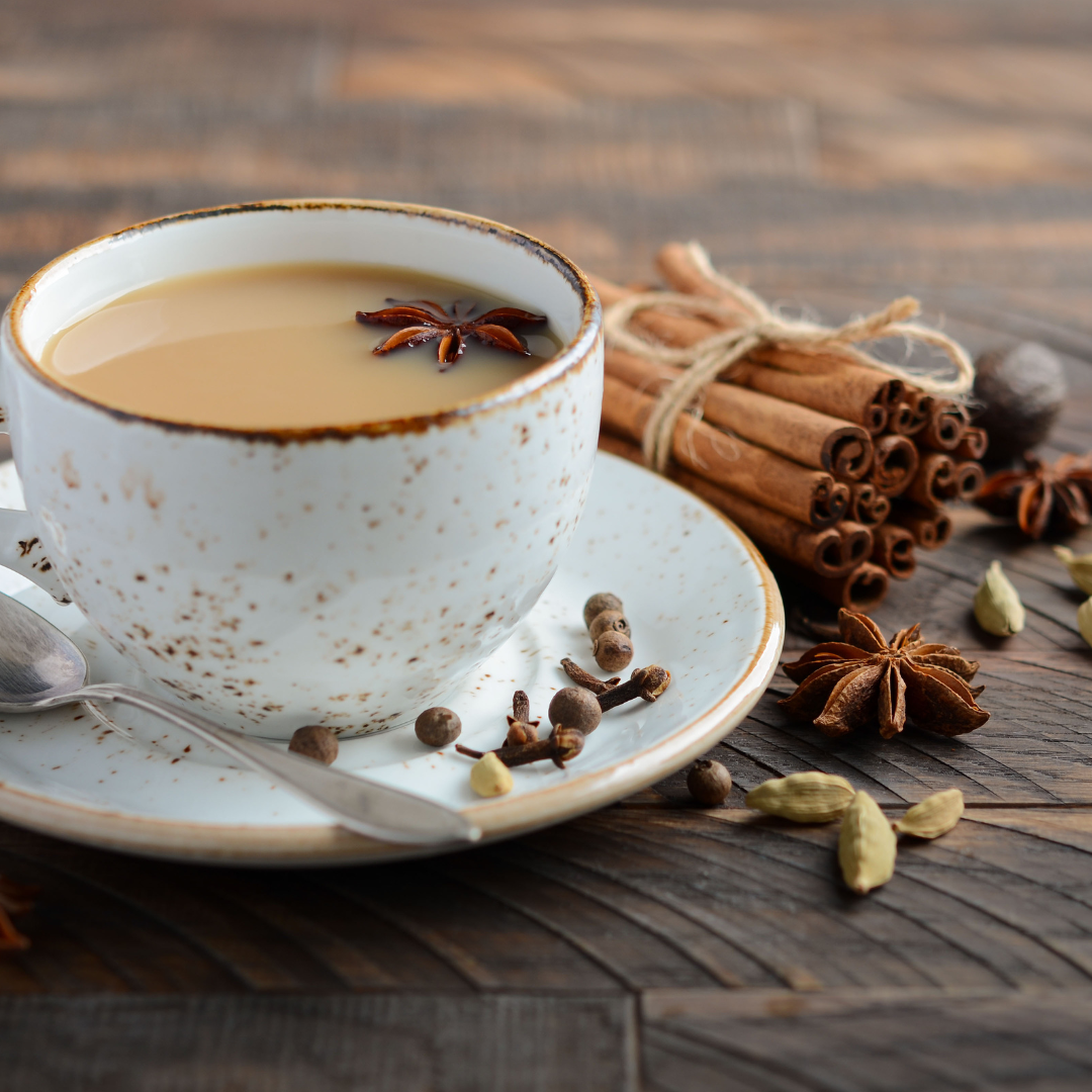 A cup of tea surrounded by cinnamon sticks, cardamom pods, dried cloves, star anise pods, and round all spice berries