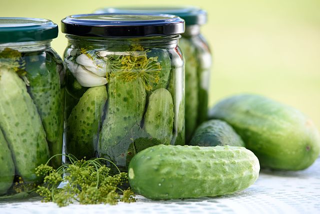 Jars of dill pickles, with cucumbers on a table